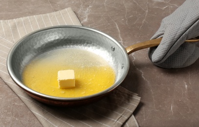 Photo of Chef holding frying pan with melting butter on grey background, closeup
