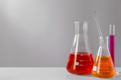 Different laboratory glassware with colorful liquids on white table against grey background. Space for text