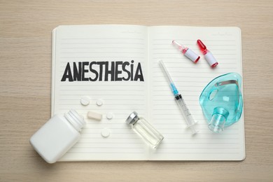 Photo of Notebook with word Anesthesia, face mask and different drugs on wooden table, top view