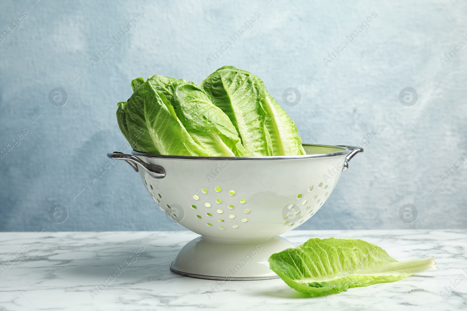 Photo of Colander with fresh ripe cos lettuce on marble table