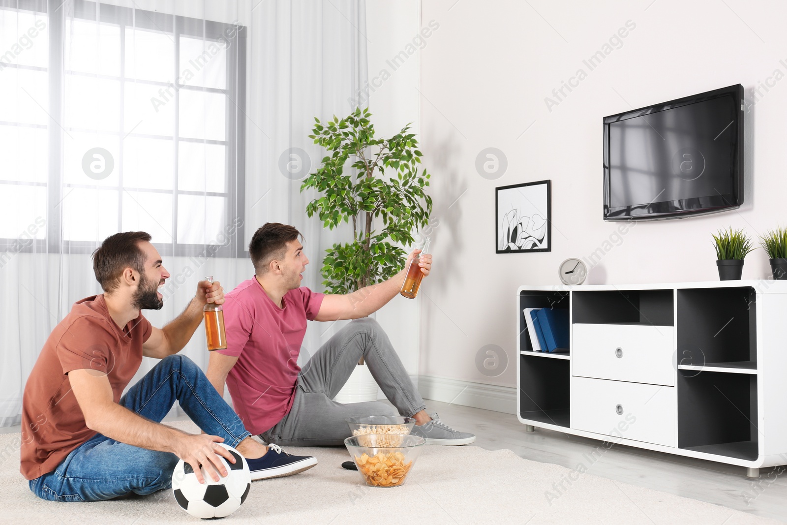 Photo of Young men watching TV while sitting on floor at home. Sport channel
