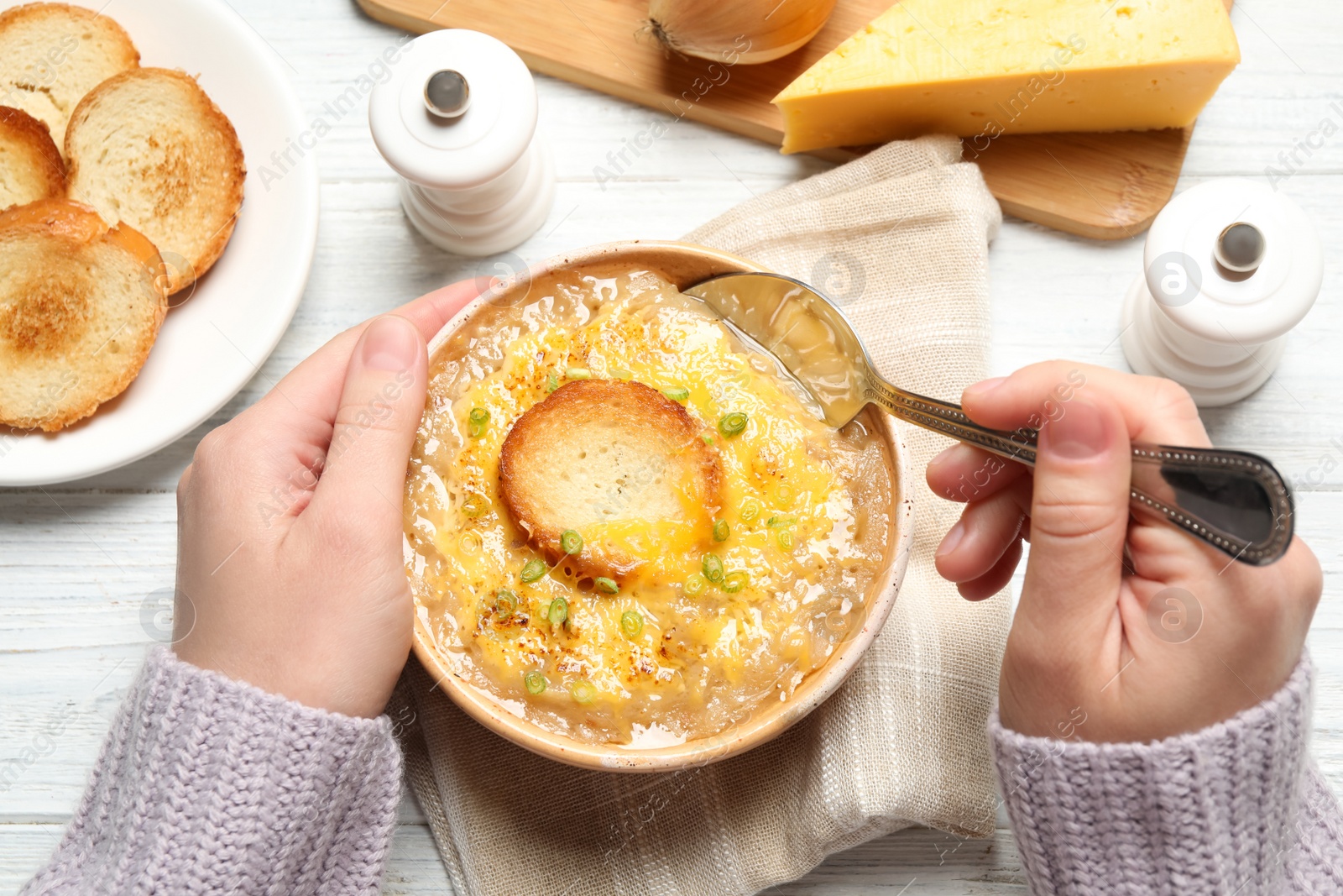 Photo of Woman eating tasty homemade french onion soup at white wooden table, top view