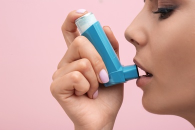 Photo of Young woman using asthma inhaler on color background, closeup