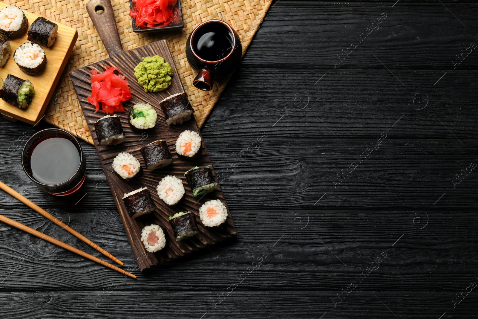 Photo of Tasty sushi rolls served on black wooden table, flat lay. Space for text