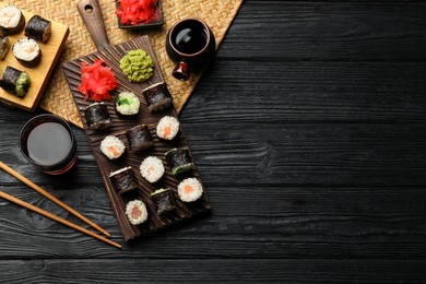 Tasty sushi rolls served on black wooden table, flat lay. Space for text