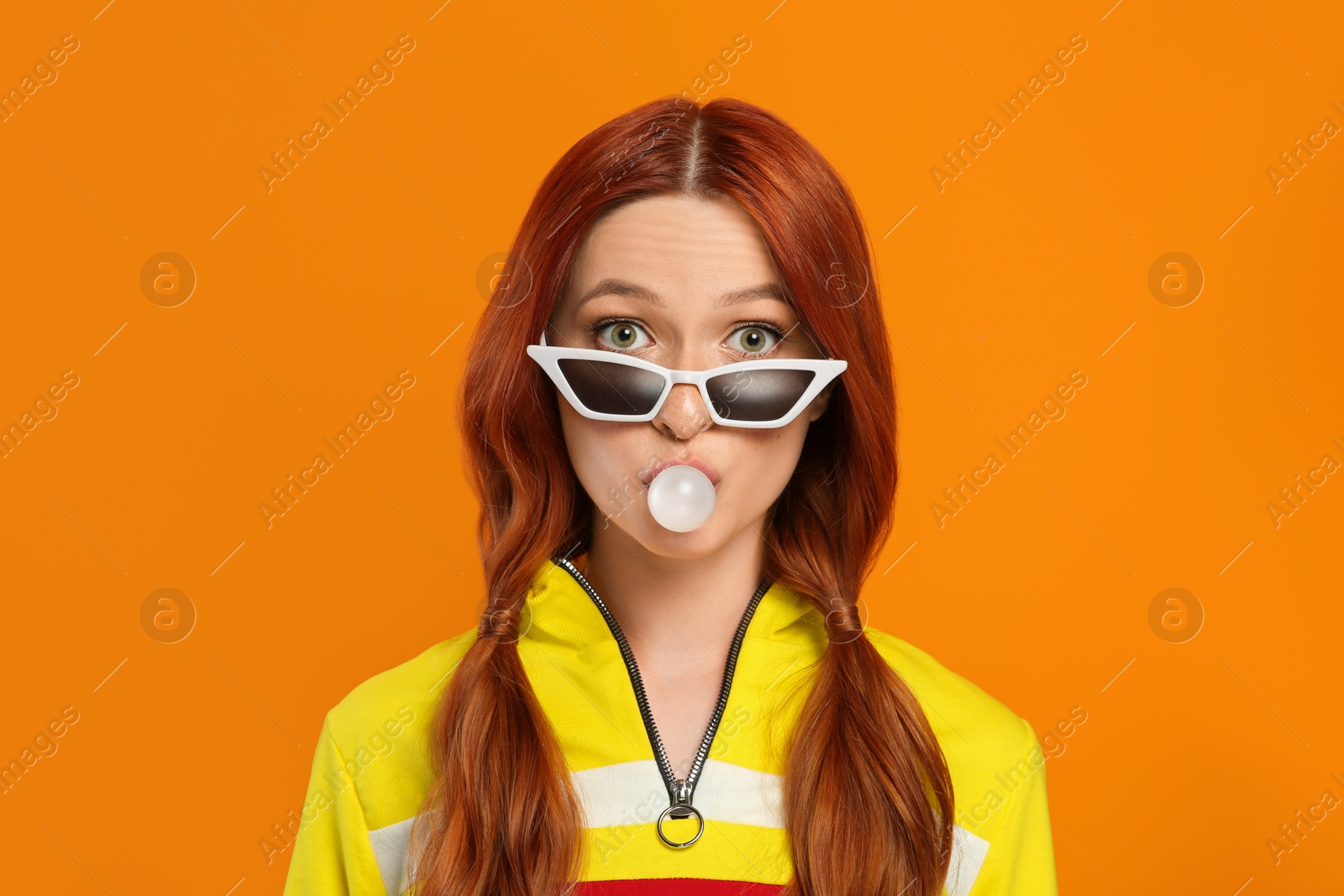 Photo of Portrait of surprised woman in sunglasses blowing bubble gum on orange background
