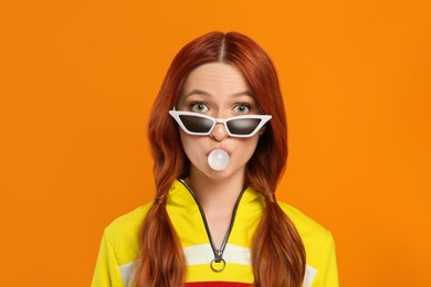 Photo of Portraitsurprised woman in sunglasses blowing bubble gum on orange background