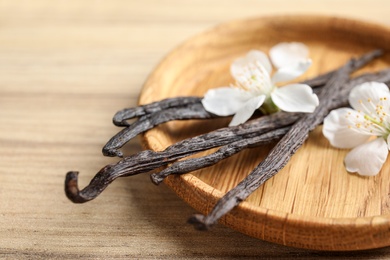 Plate with aromatic vanilla sticks and flowers on wooden background, closeup