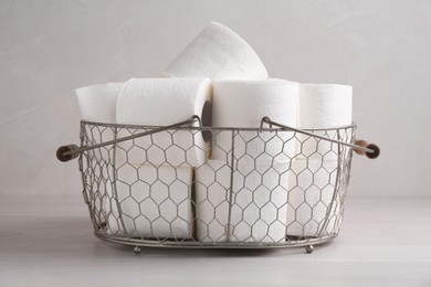 Photo of Soft toilet paper rolls in metal basket on white wooden table, closeup