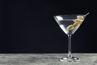 Photo of Martini cocktail with olives on grey table against dark background, space for text