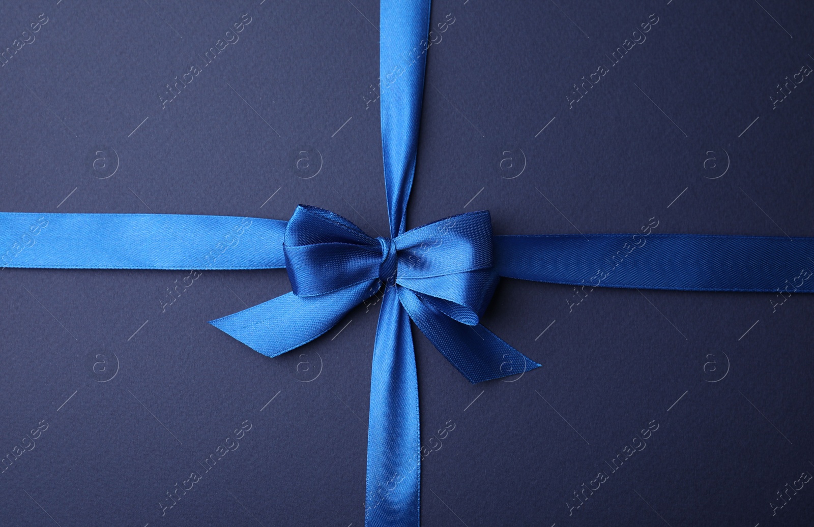 Photo of Bright satin ribbon with bow on blue background, top view