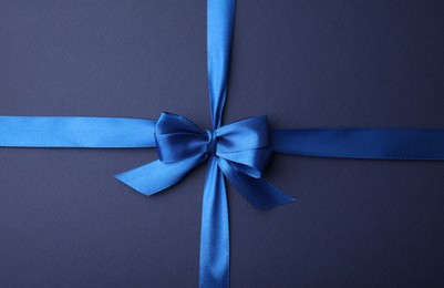 Bright satin ribbon with bow on blue background, top view