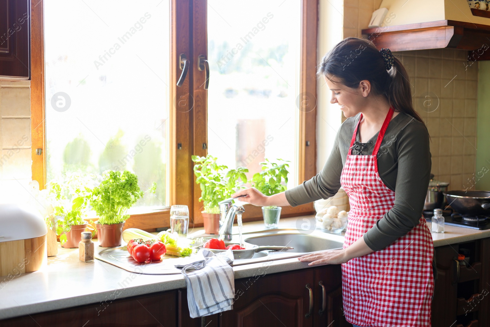 Photo of Young woman washing fresh bell peppers in kitchen sink