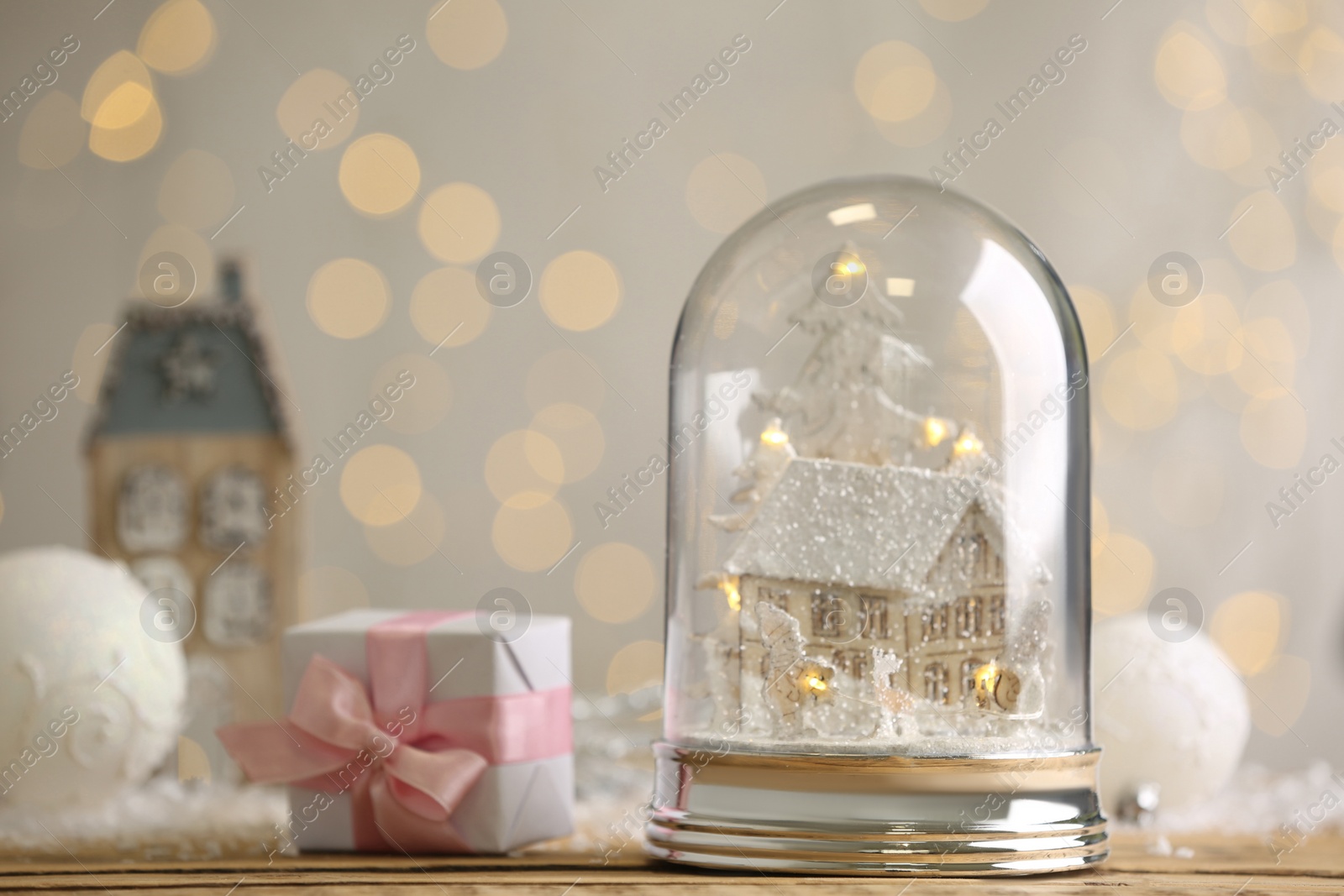 Photo of Beautiful snow globe and gift box on wooden table against blurred Christmas lights. Space for text