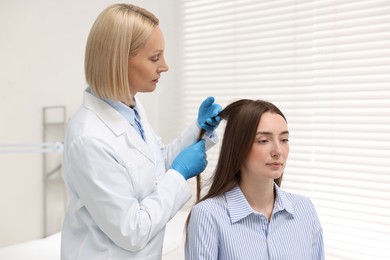 Trichologist in gloves examining patient`s hair in clinic