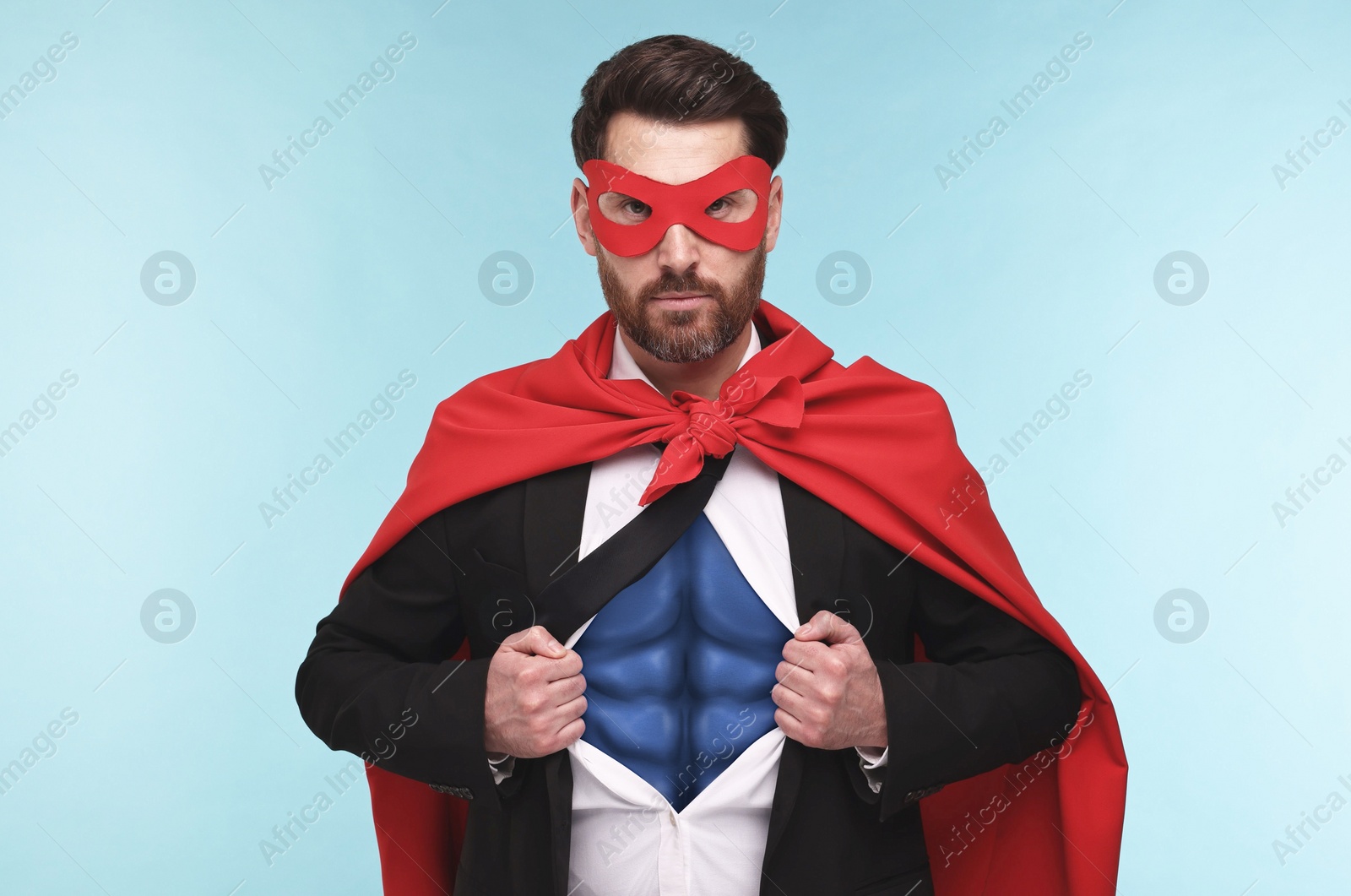 Image of Confident businessman wearing superhero costume under suit on light blue background