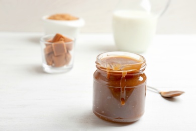 Photo of Jar of tasty caramel sauce on table, closeup. Space for text