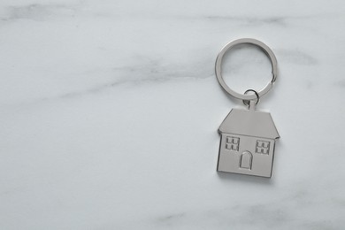 Photo of Metal keychain in shape of house on marble table, top view. Space for text