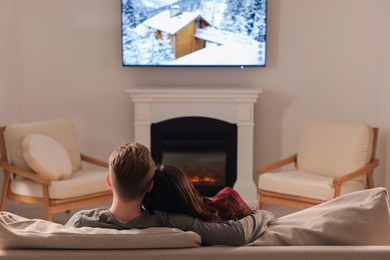 Photo of Lovely couple spending time together on sofa near fireplace at home, back view