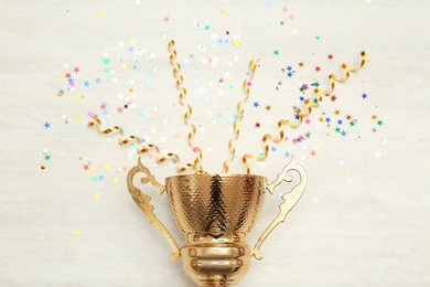 Photo of Golden trophy cup and streamers on wooden background, top view