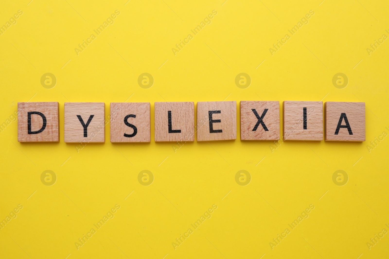 Photo of Wooden tiles with word Dyslexia on yellow background, flat lay