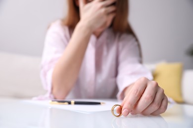 Photo of Woman with wedding ring and divorce papers at table indoors, closeup. Space for text