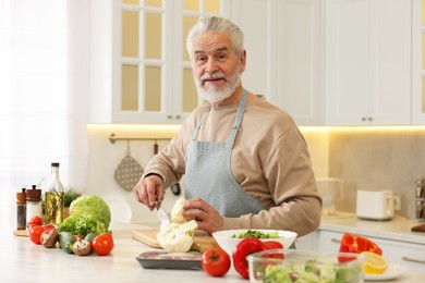 Photo of Happy man cutting cauliflower at table in kitchen