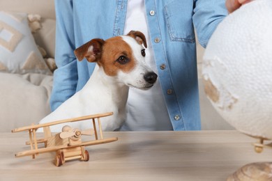 Photo of Woman at wooden table near globe, toy plane and dog indoors. Travel with pet concept
