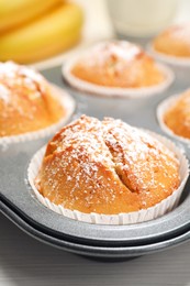 Photo of Tasty homemade banana muffins powdered with sugar in tray on white wooden table, closeup