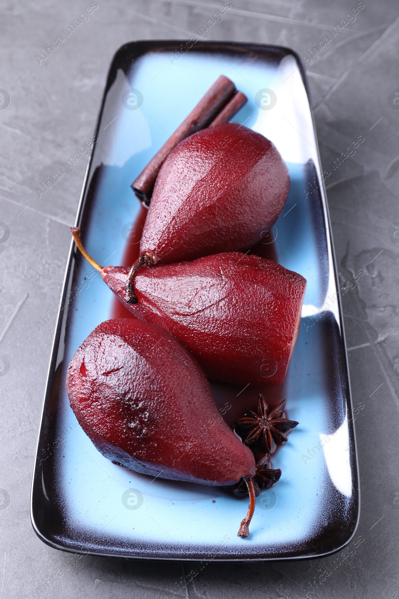 Photo of Tasty red wine poached pears and spices on grey table, closeup