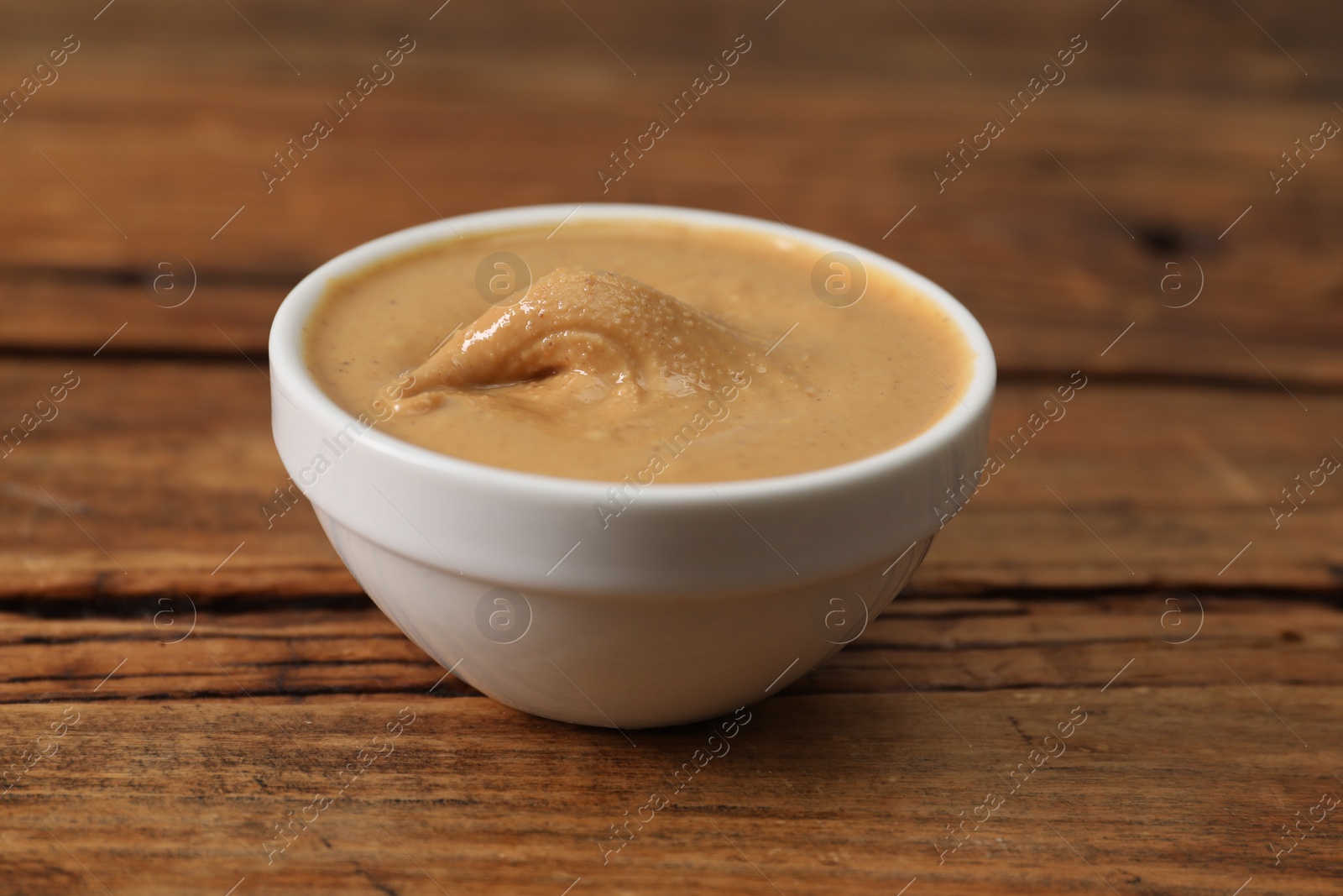 Photo of Delicious nut butter in bowl on wooden table, closeup