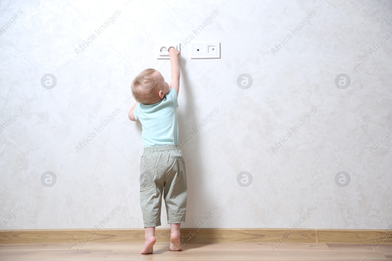 Photo of Little child playing with electrical socket indoors, back view. Dangerous situation