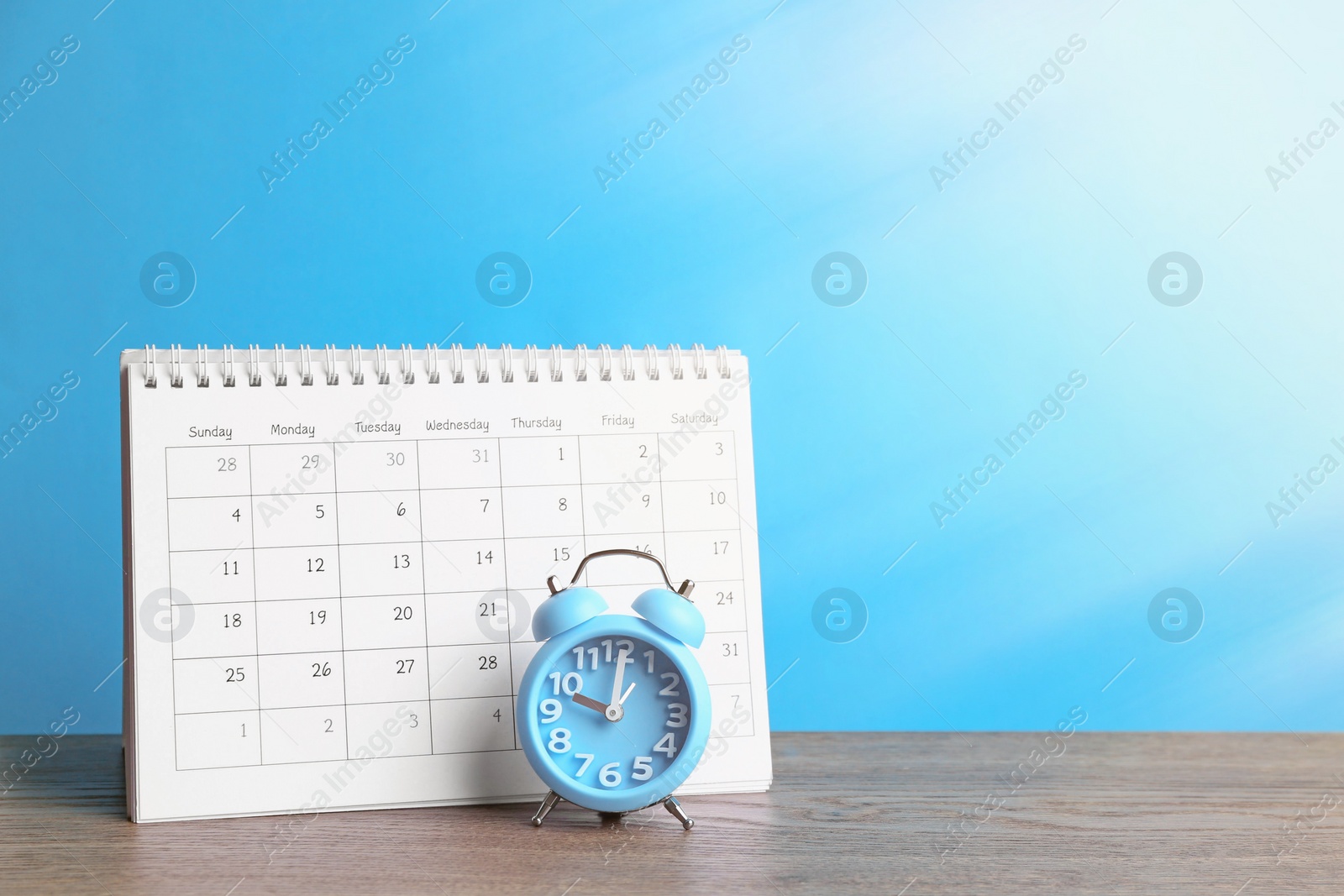 Image of Calendar and alarm clock on wooden table against light blue background. Space for text