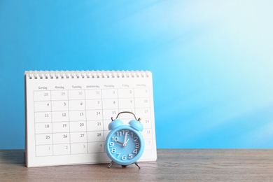 Calendar and alarm clock on wooden table against light blue background. Space for text