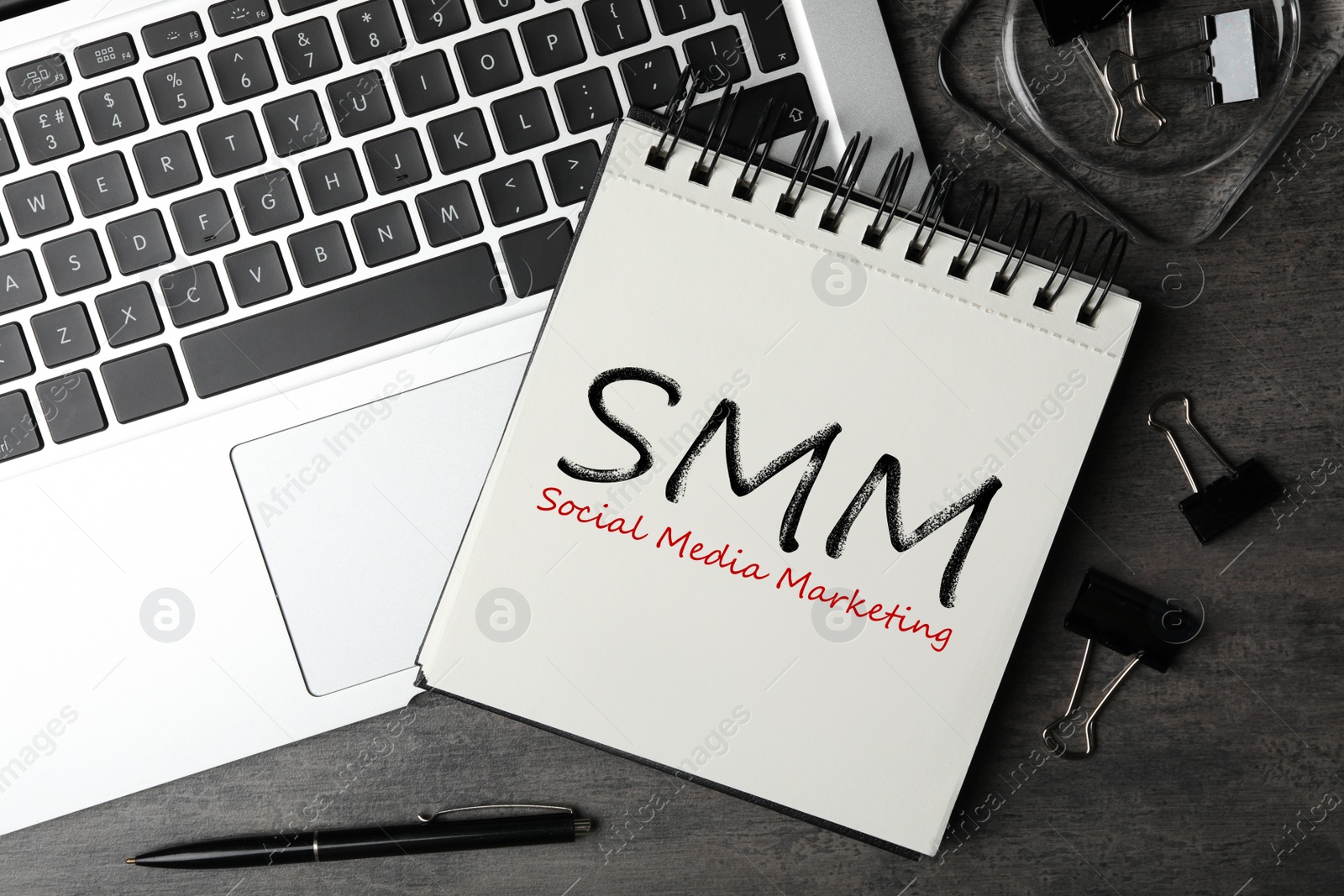 Image of Notebook with text SMM (Social media marketing) and laptop on grey table, flat lay