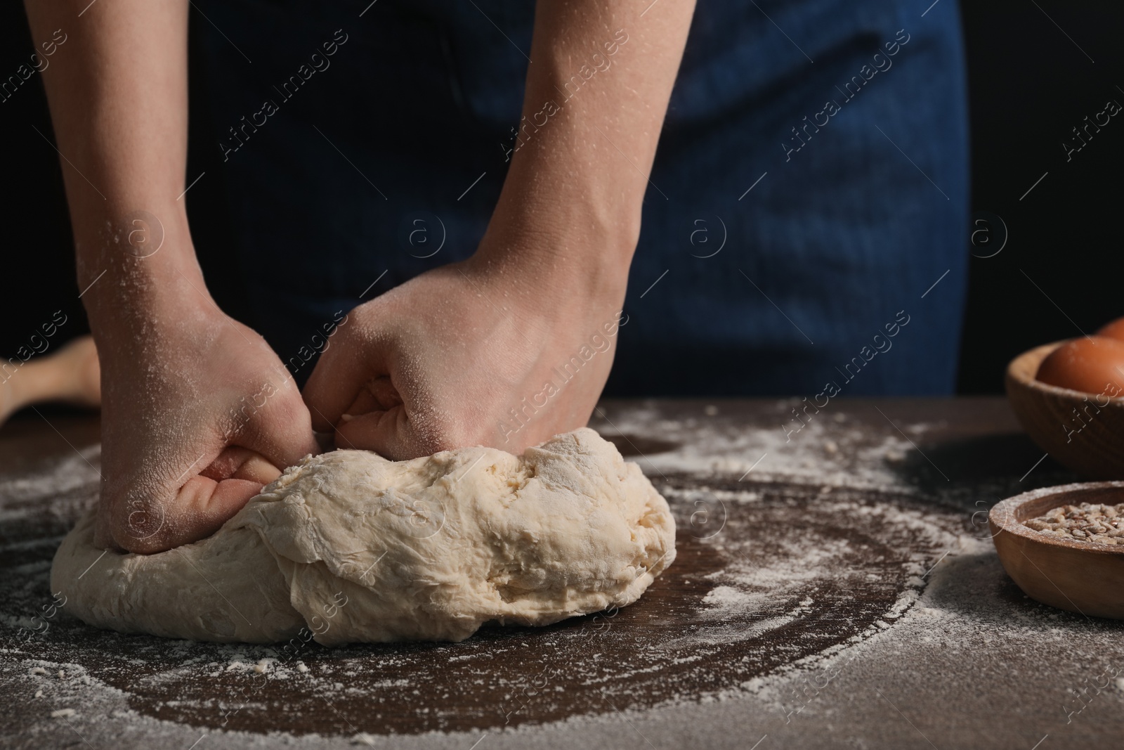 Photo of Making bread. Woman kneading dough at wooden table on dark background, closeup