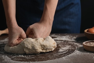 Making bread. Woman kneading dough at wooden table on dark background, closeup