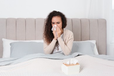 Sick African American woman with box of tissues in bed at home