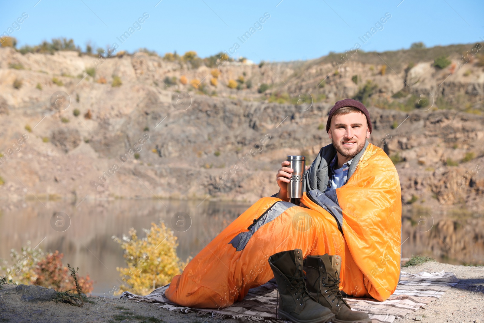 Photo of Male camper with thermos in sleeping bag outdoors. Space for text