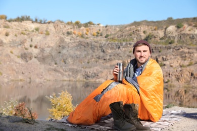 Photo of Male camper with thermos in sleeping bag outdoors. Space for text