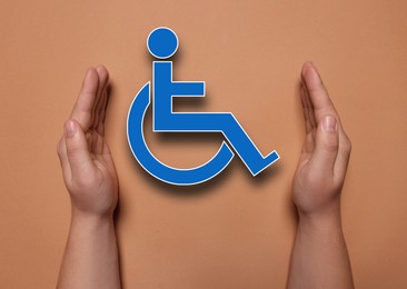 Image of Disability inclusion. Woman protecting wheelchair symbol on coral background, closeup