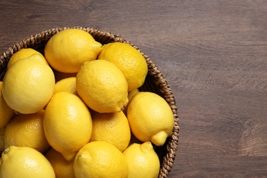 Fresh lemons in wicker basket on wooden table, top view. Space for text