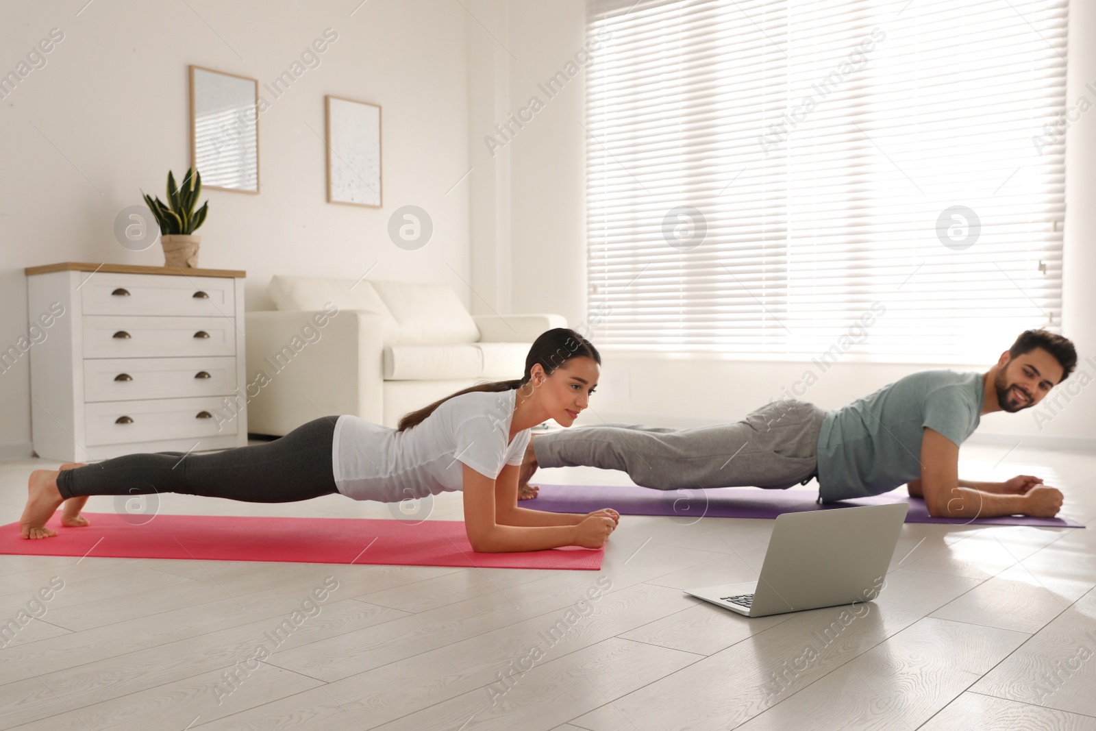 Photo of Couple practicing yoga while watching online class at home during coronavirus pandemic. Social distancing