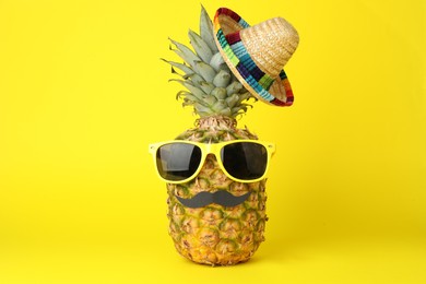 Pineapple with Mexican sombrero hat, sunglasses and fake mustache on yellow background