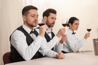 Photo of Group of people tasting red wine in glasses at table indoors. Professional butler courses
