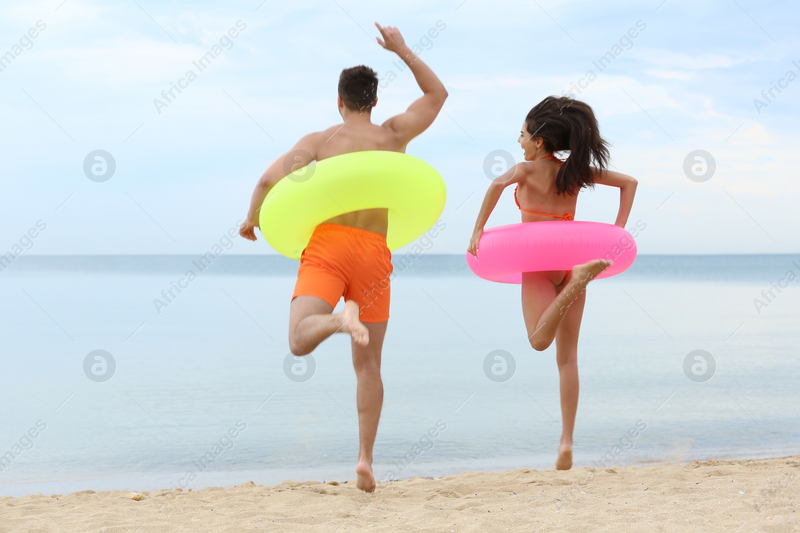 Photo of Happy young couple having fun with inflatable rings on beach near sea