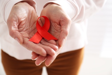 Photo of Woman holding red awareness ribbon on light background, closeup. World AIDS disease day