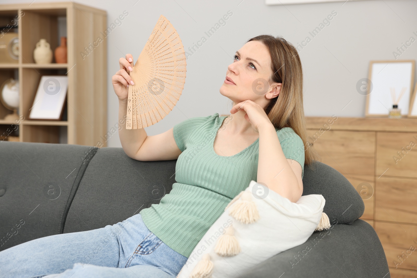 Photo of Woman waving hand fan to cool herself on sofa at home