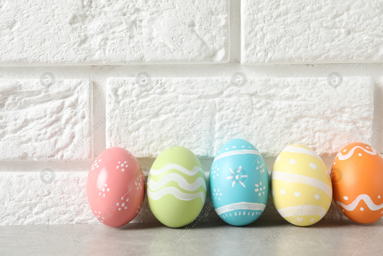 Photo of Colorful painted Easter eggs on table near brick wall, space for text