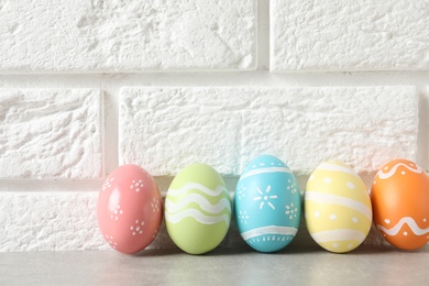 Photo of Colorful painted Easter eggs on table near brick wall, space for text